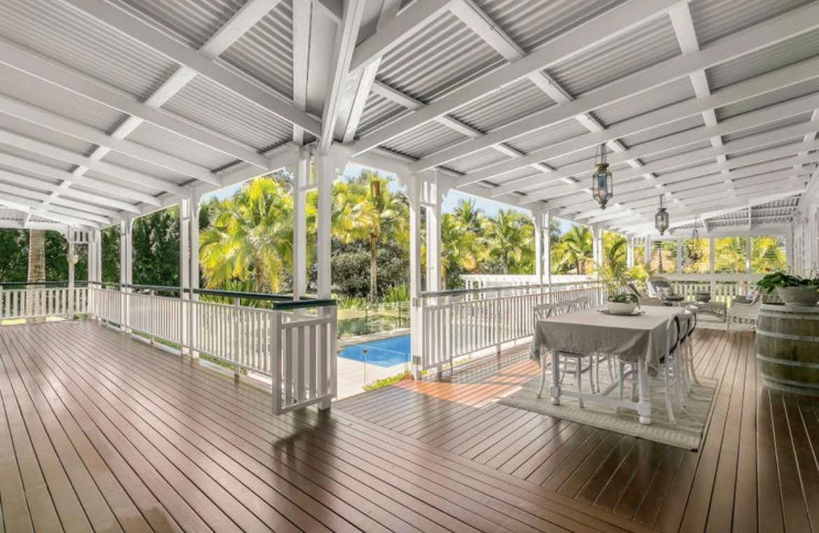 Wide Queenslander verandah with white balustrades, a stained timber floor and a pool beyond