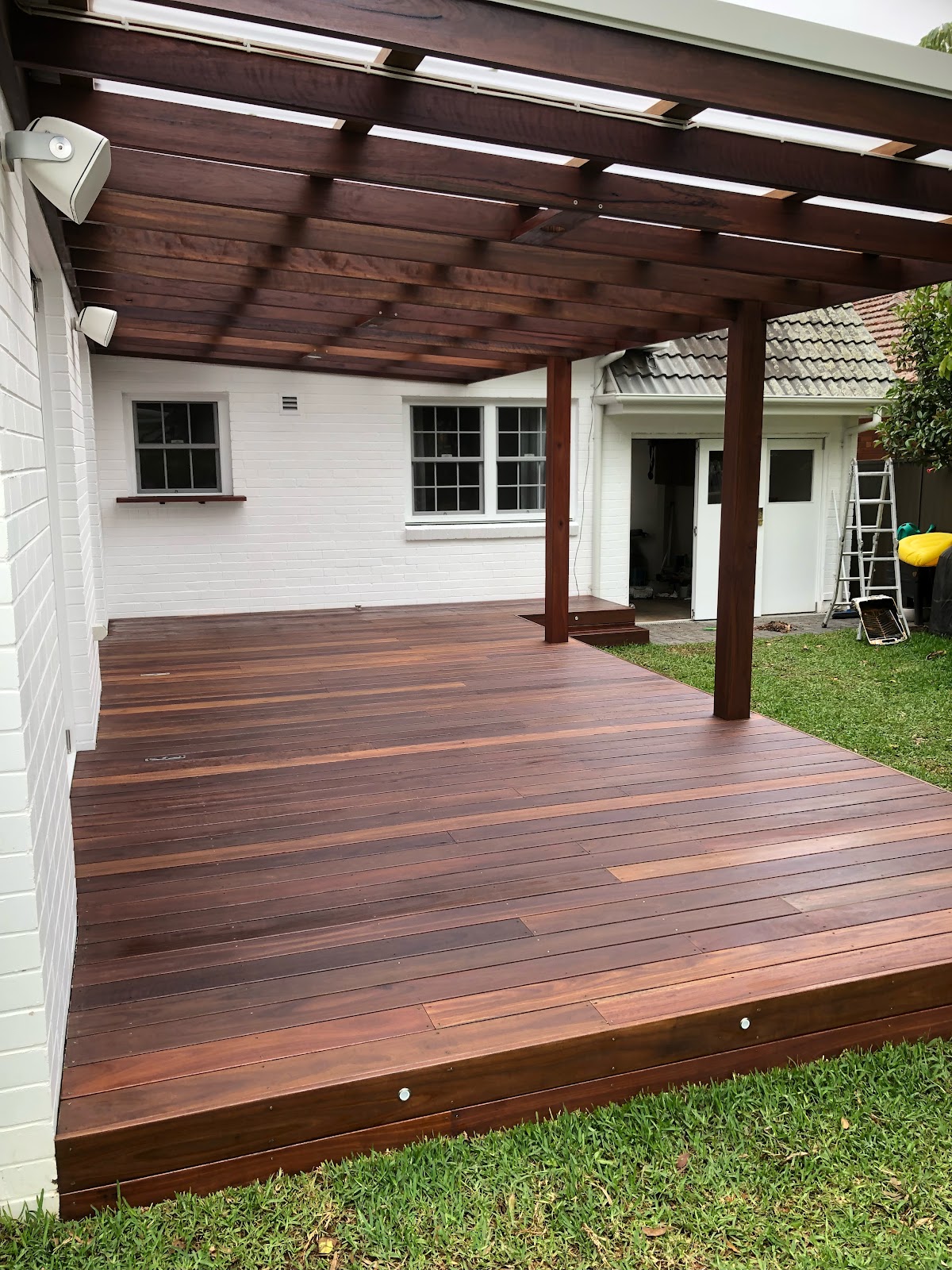 Freshly stained timber deck and pergola behind a white painted brick house