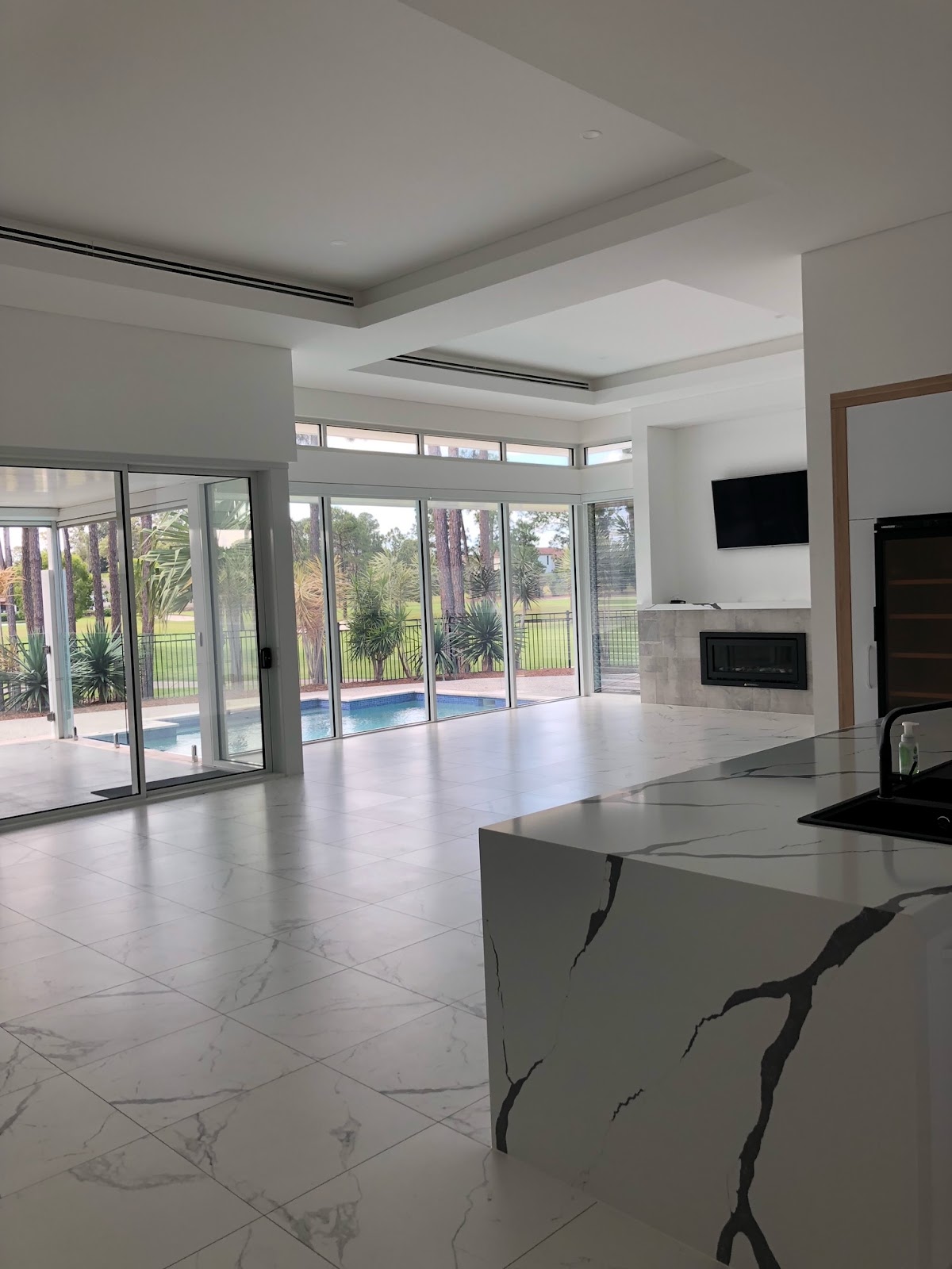 White interior with a marble island and pool beyond glass doors